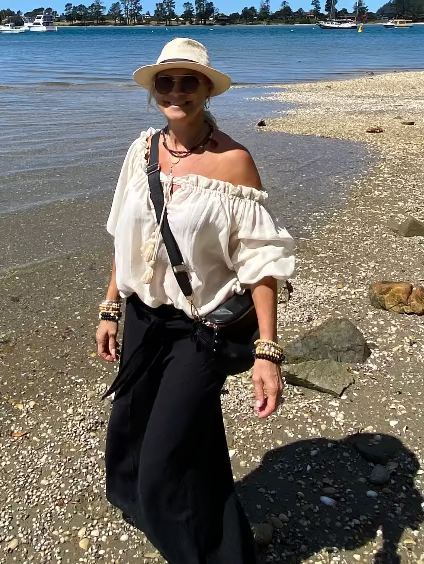 Woman wearing a white ramie peasant top and black wide leg pants, styled for warm weather resort wear by the water.